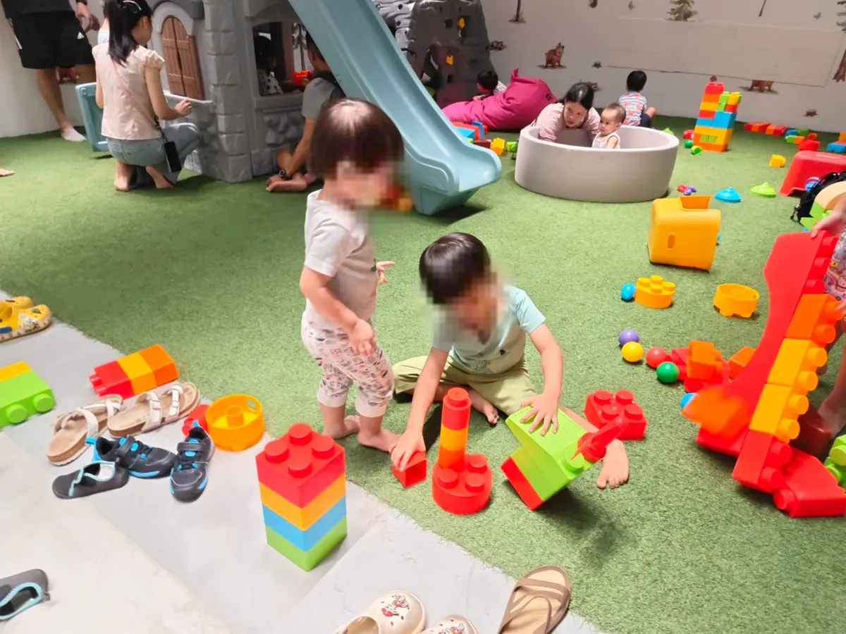 Toddlers stacking large building blocks at the free mall play area at Lentor Modern, with a castle slide behind.