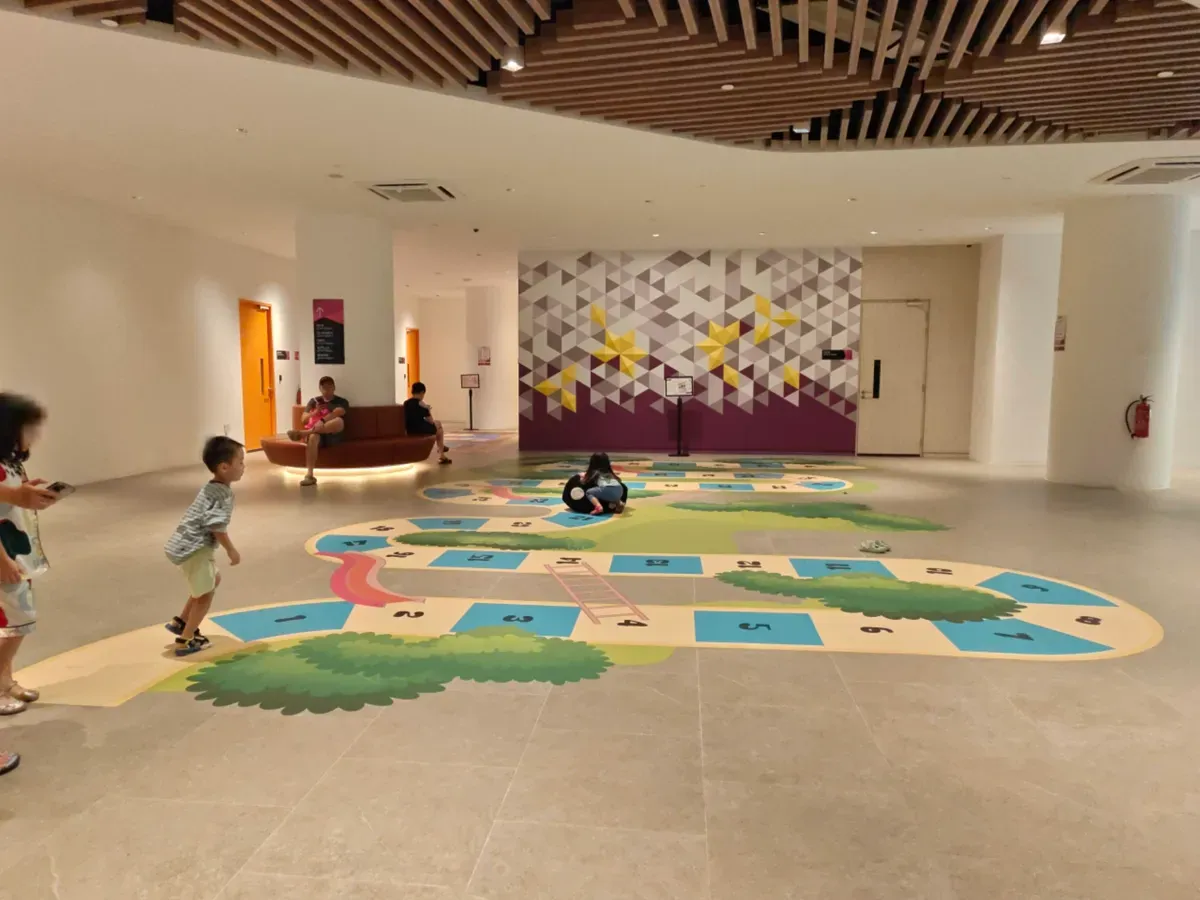 Children playing on a giant snakes-and-ladders floor game at a community club play space in Sengkang.